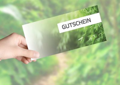 Eine Hand hält eine "GUTSCHEIN"-Geschenkkarte für das Therapiezentrum Reform inmitten grüner Blätter.