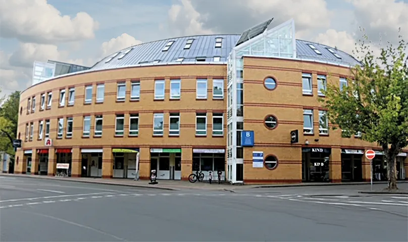 Dreistöckiges modernes Backsteingebäude mit geschwungener Fassade, großen Fenstern und Läden im Erdgeschoss an einer Straßenecke. Dreistöckiges modernes Backsteingebäude mit geschwungener Fassade, großen Fenstern und Läden im Erdgeschoss an einer Straßenecke.